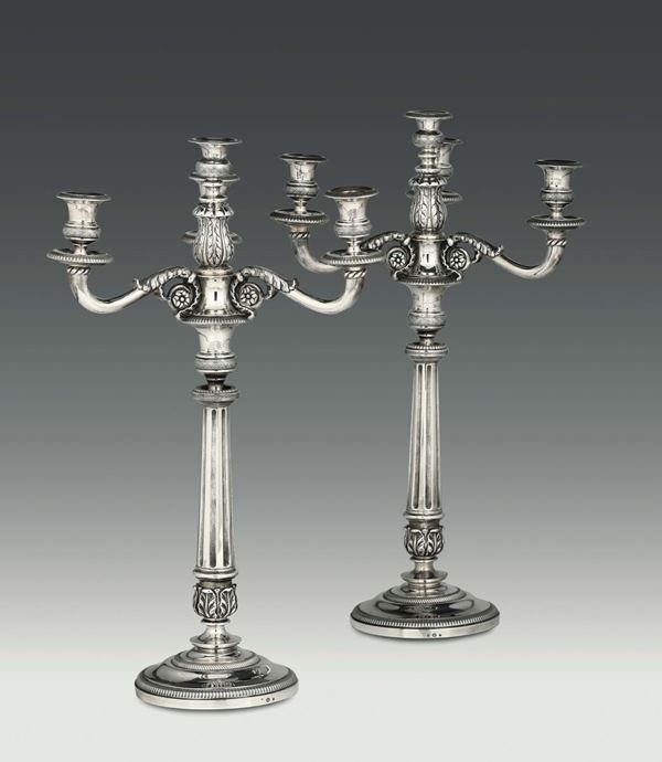 Due candelabri a quattro fiamme in argento fuso, sbalzato e cesellato, Genova, XIX secolo. Bolli di garanzia in uso dal 1824 al 1872 e dell’argentiere IR non identificato.