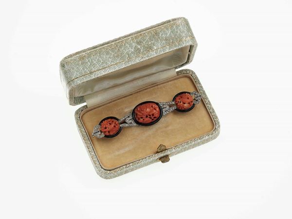Carved coral, enamel and platinum brooch. Fitted case